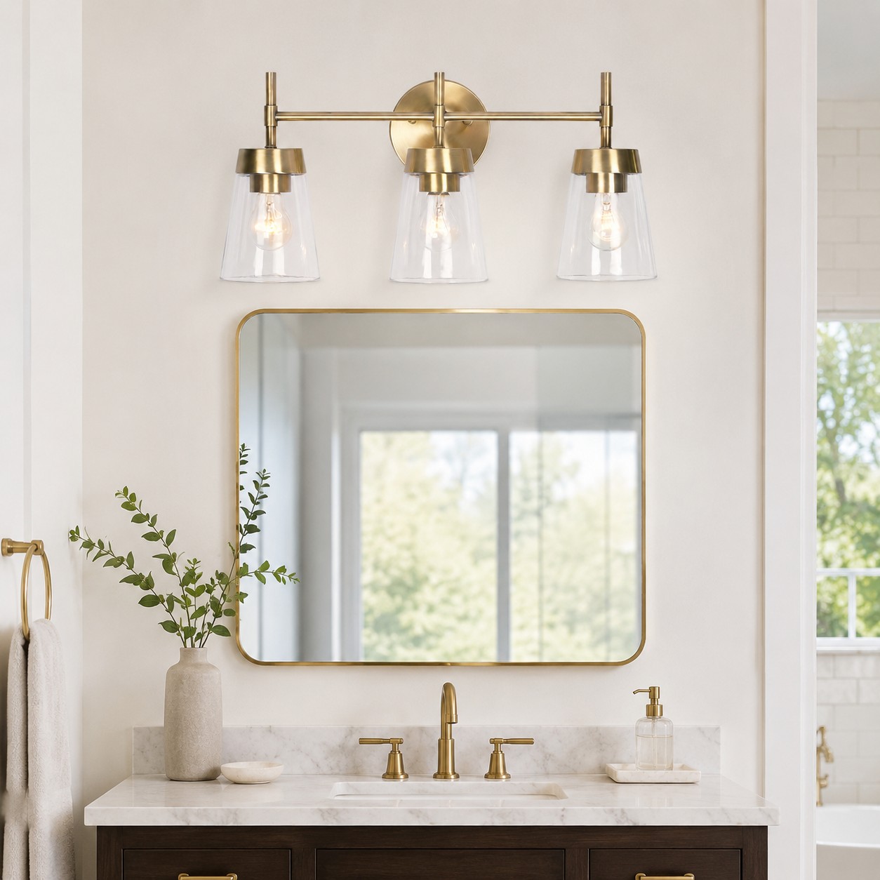 Three-light brushed brass vanity fixture installed above a bathroom mirror